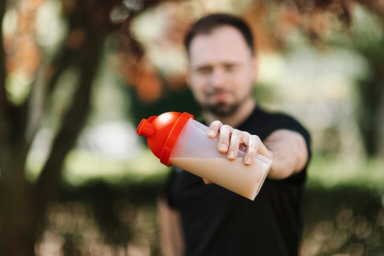 Man presenting a protein shake in a plastic tumbler against a blurred nature background.